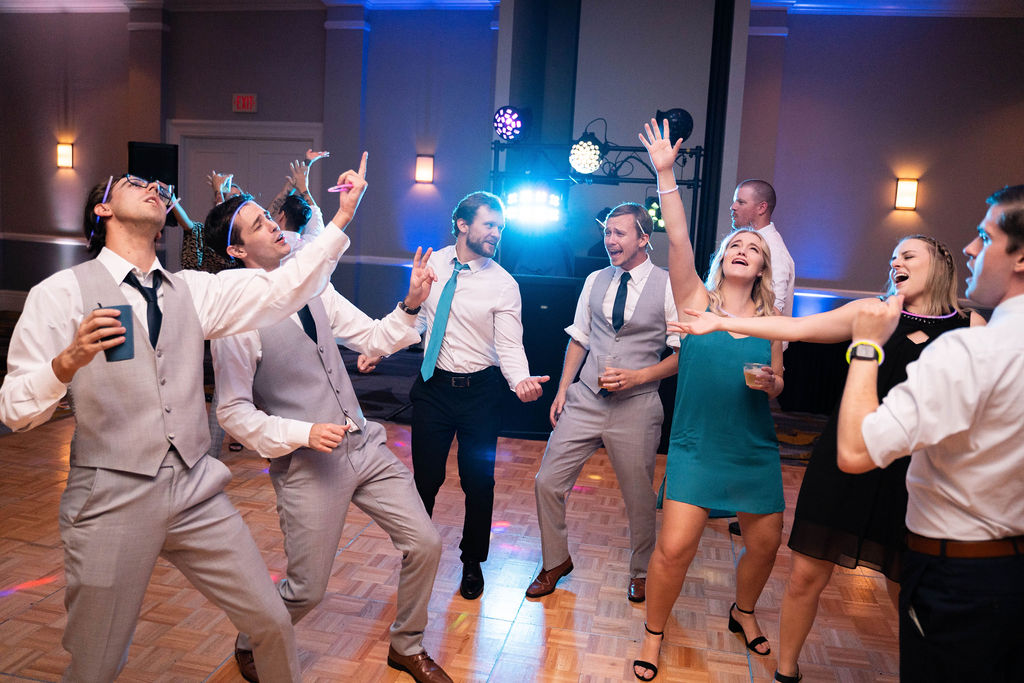 groomsmen and wedding guests singing along to a song during a wedding reception